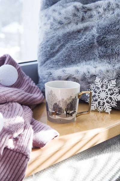 Geyiklerin içinde altın ve beyaz kış fincanı. Pencere kenarında çay ya da kahve, süveterin yanında, kış süslemesi.