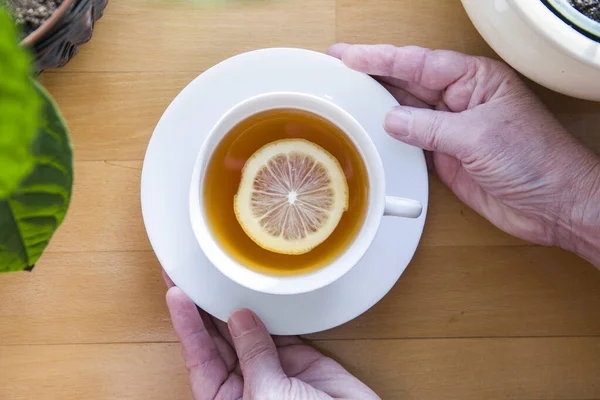 Beyaz bir fincan limonlu çay tutan insan elleri. Düz görünüm