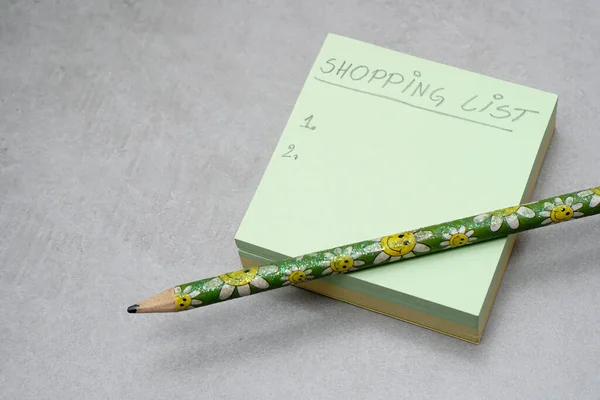 A Post-it Yapışkan Notlar 'da el yazısıyla yazılmış bir alışveriş listesi. Yeşil kare şekilli not defteri. Gri arkaplan. Organizasyon konsepti. Alışveriş planlama konsepti.