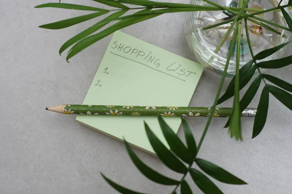A Post-it Yapışkan Notlar 'da el yazısıyla yazılmış bir alışveriş listesi. Yeşil kare notlar. Yeşil yapraklar ve gri arka plan. Organizasyon konsepti. Alışveriş planlama konsepti.