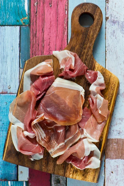 Prosciutto fatiado em uma placa de corte de madeira e fundo de madeira enferrujado — Fotografia de Stock