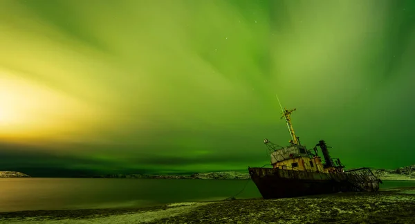 Abandoned boat on the Barents Sea beach in Teriberka, Russia. A cloudy sky illuminated by the northern lights — Stock Photo, Image