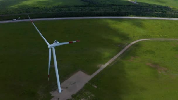 Vista aérea de um campo verde em frente a turbinas eólicas que produzem energia renovável limpa. — Vídeo de Stock