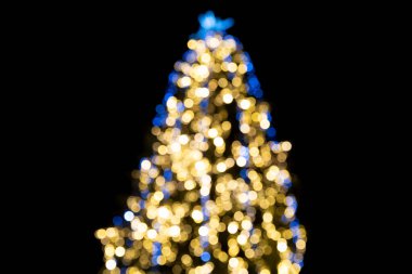 Güzel bulanık bir Noel ağacı. Sıcak altın ve serin mavi ışıklarla süslenmiş. Bokeh etkisi, koyu arkaplan..