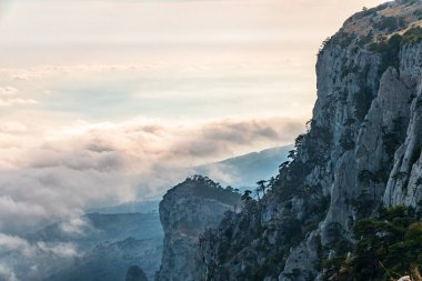Kayalık dağların, sisli ve bulutlu vadinin görkemli manzarası. Kremalı sis dağ vadisini gün batımıyla kapladı. Kırım Dağları üzerinde puslu gün batımı. Konum Ai-Petri, Kırım.