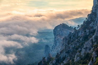 Kayalık dağların, sisli ve bulutlu vadinin görkemli manzarası. Kremalı sis dağ vadisini gün batımıyla kapladı. Kırım Dağları üzerinde puslu gün batımı. Konum Ai-Petri, Kırım.