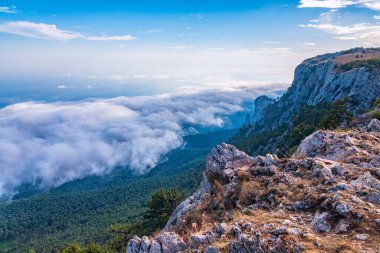 Kayalık dağların, sisli ve bulutlu vadinin görkemli manzarası. Kremalı sis dağ vadisini gün batımıyla kapladı. Kırım Dağları üzerinde puslu gün batımı. Konum Ai-Petri, Kırım.