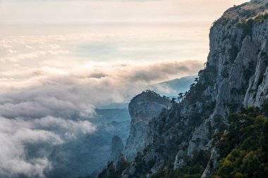 Kayalık dağların, sisli ve bulutlu vadinin görkemli manzarası. Kremalı sis dağ vadisini gün batımıyla kapladı. Kırım Dağları üzerinde puslu gün batımı. Konum Ai-Petri, Kırım.
