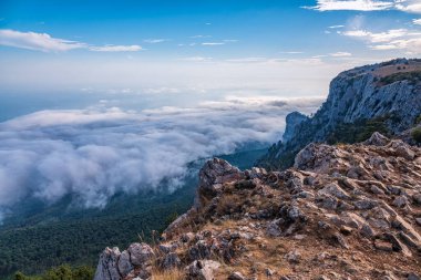 Kayalık dağların, sisli ve bulutlu vadinin görkemli manzarası. Kremalı sis dağ vadisini gün batımıyla kapladı. Kırım Dağları üzerinde puslu gün batımı. Konum Ai-Petri, Kırım.
