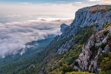 Kayalık dağların, sisli ve bulutlu vadinin görkemli manzarası. Kremalı sis dağ vadisini gün batımıyla kapladı. Kırım Dağları üzerinde puslu gün batımı. Konum Ai-Petri, Kırım.