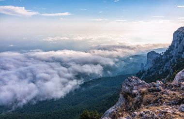Kayalık dağların, sisli ve bulutlu vadinin görkemli manzarası. Kremalı sis dağ vadisini gün batımıyla kapladı. Kırım Dağları üzerinde puslu gün batımı. Konum Ai-Petri, Kırım.
