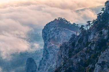 Kayalık dağların, sisli ve bulutlu vadinin görkemli manzarası. Kremalı sis dağ vadisini gün batımıyla kapladı. Kırım Dağları üzerinde puslu gün batımı. Konum Ai-Petri, Kırım.