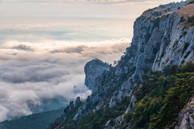 Kayalık dağların, sisli ve bulutlu vadinin görkemli manzarası. Kremalı sis dağ vadisini gün batımıyla kapladı. Kırım Dağları üzerinde puslu gün batımı. Konum Ai-Petri, Kırım.