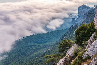 Kayalık dağların, sisli ve bulutlu vadinin görkemli manzarası. Kremalı sis dağ vadisini gün batımıyla kapladı. Kırım Dağları üzerinde puslu gün batımı. Konum Ai-Petri, Kırım.