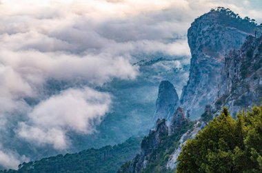 Kayalık dağların, sisli ve bulutlu vadinin görkemli manzarası. Kremalı sis dağ vadisini gün batımıyla kapladı. Kırım Dağları üzerinde puslu gün batımı. Konum Ai-Petri, Kırım.