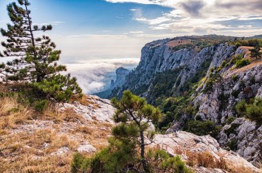 Kayalık dağların, sisli ve bulutlu vadinin görkemli manzarası. Kremalı sis dağ vadisini gün batımıyla kapladı. Kırım Dağları üzerinde puslu gün batımı. Konum Ai-Petri, Kırım.