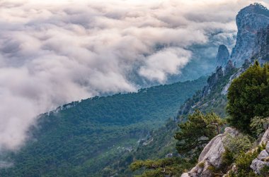 Kayalık dağların, sisli ve bulutlu vadinin görkemli manzarası. Kremalı sis dağ vadisini gün batımıyla kapladı. Kırım Dağları üzerinde puslu gün batımı. Konum Ai-Petri, Kırım.