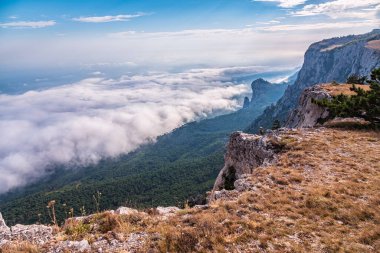 Kayalık dağların, sisli ve bulutlu vadinin görkemli manzarası. Kremalı sis dağ vadisini gün batımıyla kapladı. Kırım Dağları üzerinde puslu gün batımı. Konum Ai-Petri, Kırım.
