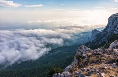 Kayalık dağların, sisli ve bulutlu vadinin görkemli manzarası. Kremalı sis dağ vadisini gün batımıyla kapladı. Kırım Dağları üzerinde puslu gün batımı. Konum Ai-Petri, Kırım.
