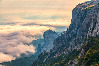 Kayalık dağların, sisli ve bulutlu vadinin görkemli manzarası. Kremalı sis dağ vadisini gün batımıyla kapladı. Kırım Dağları üzerinde puslu gün batımı. Konum Ai-Petri, Kırım.