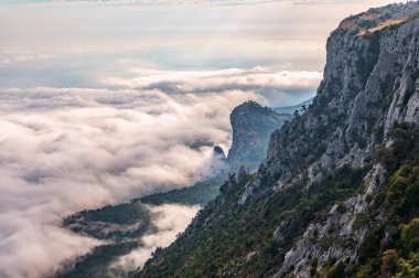 Kayalık dağların, sisli ve bulutlu vadinin görkemli manzarası. Kremalı sis dağ vadisini gün batımıyla kapladı. Kırım Dağları üzerinde puslu gün batımı. Konum Ai-Petri, Kırım.