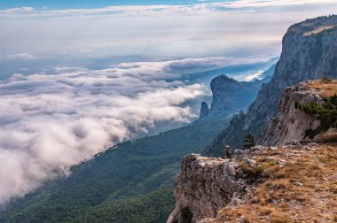 Kayalık dağların, sisli ve bulutlu vadinin görkemli manzarası. Kremalı sis dağ vadisini gün batımıyla kapladı. Kırım Dağları üzerinde puslu gün batımı. Konum Ai-Petri, Kırım.