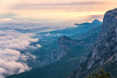 Kayalık dağların, sisli ve bulutlu vadinin görkemli manzarası. Kremalı sis dağ vadisini gün batımıyla kapladı. Kırım Dağları üzerinde puslu gün batımı. Konum Ai-Petri, Kırım.