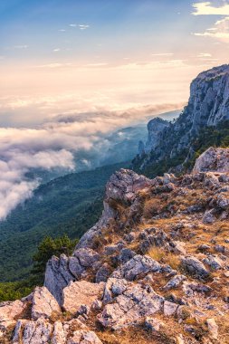 Kayalık dağların, sisli ve bulutlu vadinin görkemli manzarası. Kremalı sis dağ vadisini gün batımıyla kapladı. Kırım Dağları üzerinde puslu gün batımı. Konum Ai-Petri, Kırım.