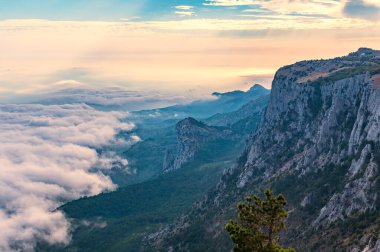 Kayalık dağların, sisli ve bulutlu vadinin görkemli manzarası. Kremalı sis dağ vadisini gün batımıyla kapladı. Kırım Dağları üzerinde puslu gün batımı. Konum Ai-Petri, Kırım.