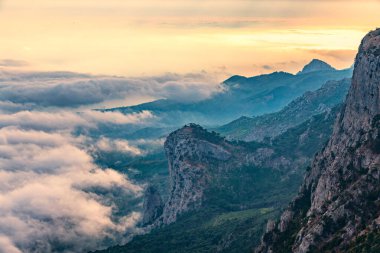 Çok katmanlı kayalık dağların, sisli ve bulutlu vadinin görkemli manzarası. Kremalı sis dağ vadisini gün batımıyla kapladı. Kırım Dağları üzerinde puslu gün batımı. Konum Ai-Petri, Kırım