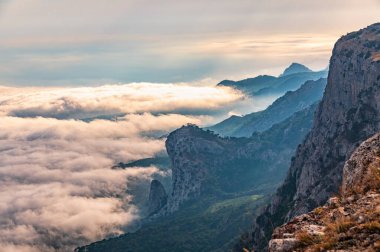 Kayalık dağların, sisli ve bulutlu vadinin görkemli manzarası. Kremalı sis dağ vadisini gün batımıyla kapladı. Kırım Dağları üzerinde puslu gün batımı. Konum Ai-Petri, Kırım.