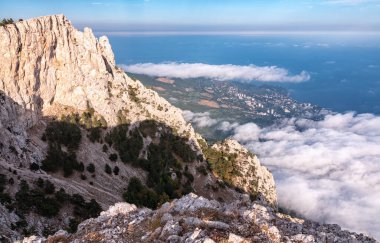 Yüksek taş kaya ve deniz kıyısı alçak bulutlar ve sisli günbatımında meskun binalar. Deniz kıyısındaki kayalık dağ. Yalta, Kırım