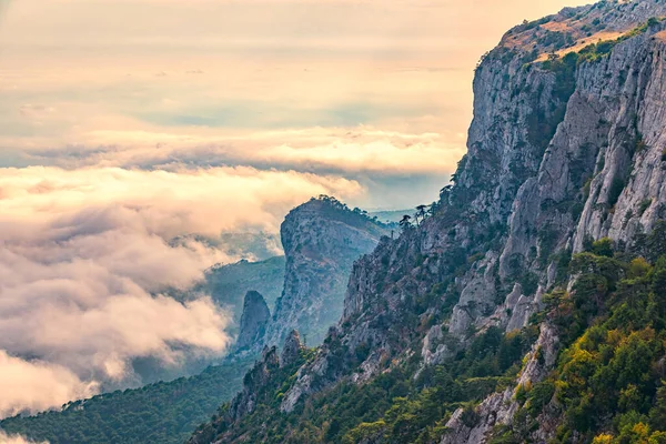 Kayalık dağların, sisli ve bulutlu vadinin görkemli manzarası. Kremalı sis dağ vadisini gün batımıyla kapladı. Kırım Dağları üzerinde puslu gün batımı. Konum Ai-Petri, Kırım.