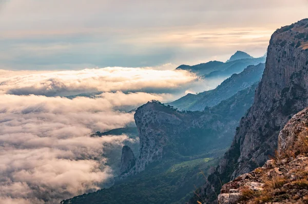 Kayalık dağların, sisli ve bulutlu vadinin görkemli manzarası. Kremalı sis dağ vadisini gün batımıyla kapladı. Kırım Dağları üzerinde puslu gün batımı. Konum Ai-Petri, Kırım.