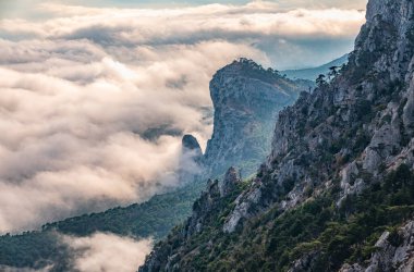 Kayalık dağların, sisli ve bulutlu vadinin görkemli manzarası. Kremalı sis dağ vadisini gün batımıyla kapladı. Kırım Dağları üzerinde puslu gün batımı. Konum Ai-Petri, Kırım.