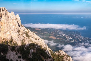 Yüksek taş kaya ve deniz kıyısı alçak bulutlar ve sisli günbatımında meskun binalar. Deniz kıyısındaki kayalık dağ. Yalta, Kırım
