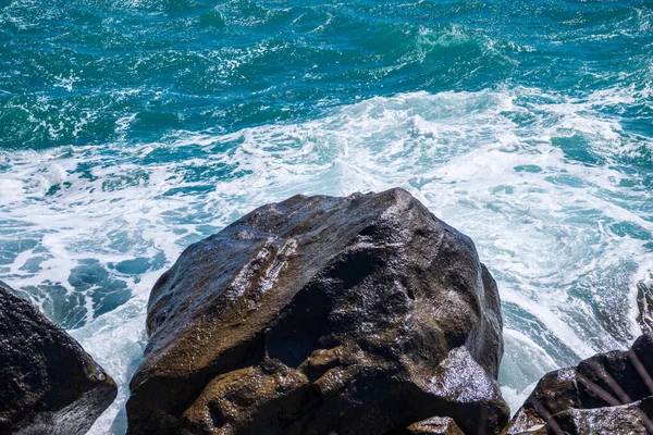 Sea water beats against rocks. Sea waves of dark water beat against the coastal rocks. An infinite number of splashes, drops of water and white foam are scattered.