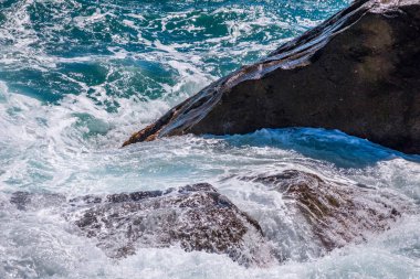 Deniz suyu kayalara çarpar. Deniz dalgaları kıyıdaki kayalara vuruyor. Sonsuz sayıda sıçrama, su damlası ve beyaz köpük dağılmış..