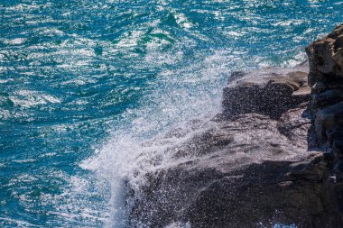 Deniz suyu kayalara çarpar. Deniz dalgaları kıyıdaki kayalara vuruyor. Sonsuz sayıda sıçrama, su damlası ve beyaz köpük dağılmış..