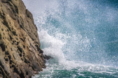 Deniz suyu kayalara çarpar. Deniz dalgaları kıyıdaki kayalara vuruyor. Sonsuz sayıda sıçrama, su damlası ve beyaz köpük dağılmış..