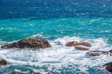 Deniz suyu kayalara çarpar. Deniz dalgaları kıyıdaki kayalara vuruyor. Sonsuz sayıda sıçrama, su damlası ve beyaz köpük dağılmış..