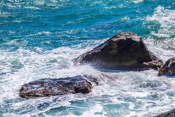 Sea water beats against rocks. Sea waves of dark water beat against the coastal rocks. An infinite number of splashes, drops of water and white foam are scattered.