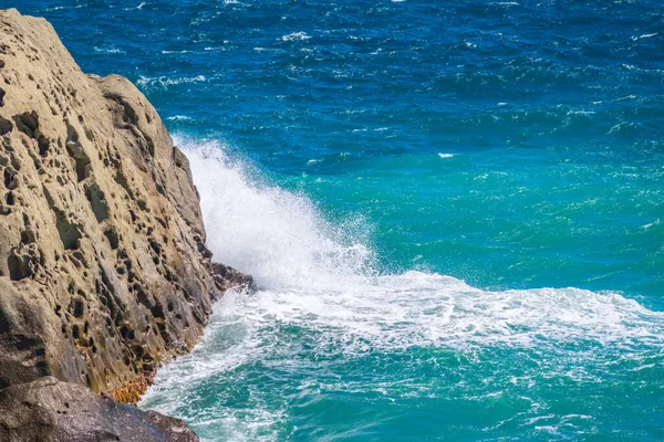 Sea water beats against rocks. Sea waves of dark water beat against the coastal rocks. An infinite number of splashes, drops of water and white foam are scattered.