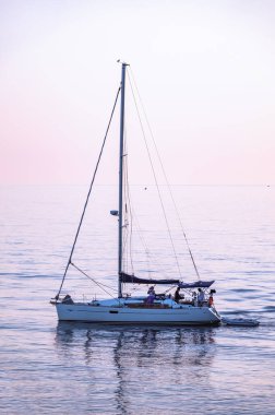 Güzel pembe günbatımında mavi denizde yelken açmak. Huzurlu sularda bir yat.