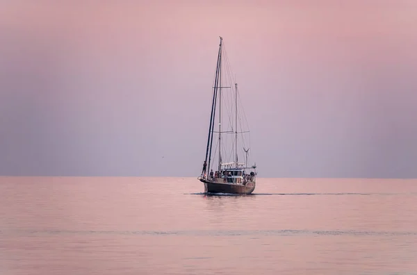 Güzel pembe günbatımında mavi denizde yelken açmak. Huzurlu sularda bir yat.