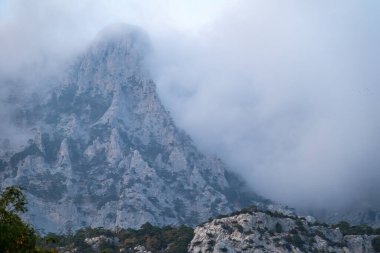 Ormanlık yamaçları ve tepeleri bulutların arasına gizlenmiş yüksek kayalık dağlar. Bulutlu bir günde dağlarda yoğun sis var. Ai-Petri, Kırım