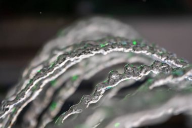 Koyu arkaplandaki çeşmeden su fışkırıyor. Sadece çeşme suyunun doğal dokusu. Yüksek dalgalar sıcak yaz aylarında fotokopi uzayını etkiler. Güneşli bir günde su püskürtür. Yakın plan..