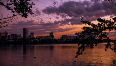 Şehirde günbatımı gökyüzü. Suda gün batımının yansımaları, batan güneş ve gökyüzü nehre yansıyor, gün batımında şehir, sudaki binaların yansıması.