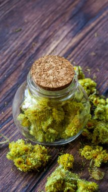 Ahşap bir arka planda cam bir kavanozdaki sarı ölümsüzlük çiçekleri.