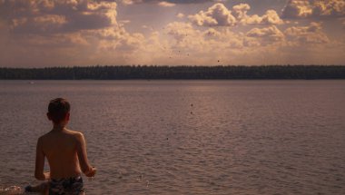 Çocuk denizde gün batımını izliyor.        
